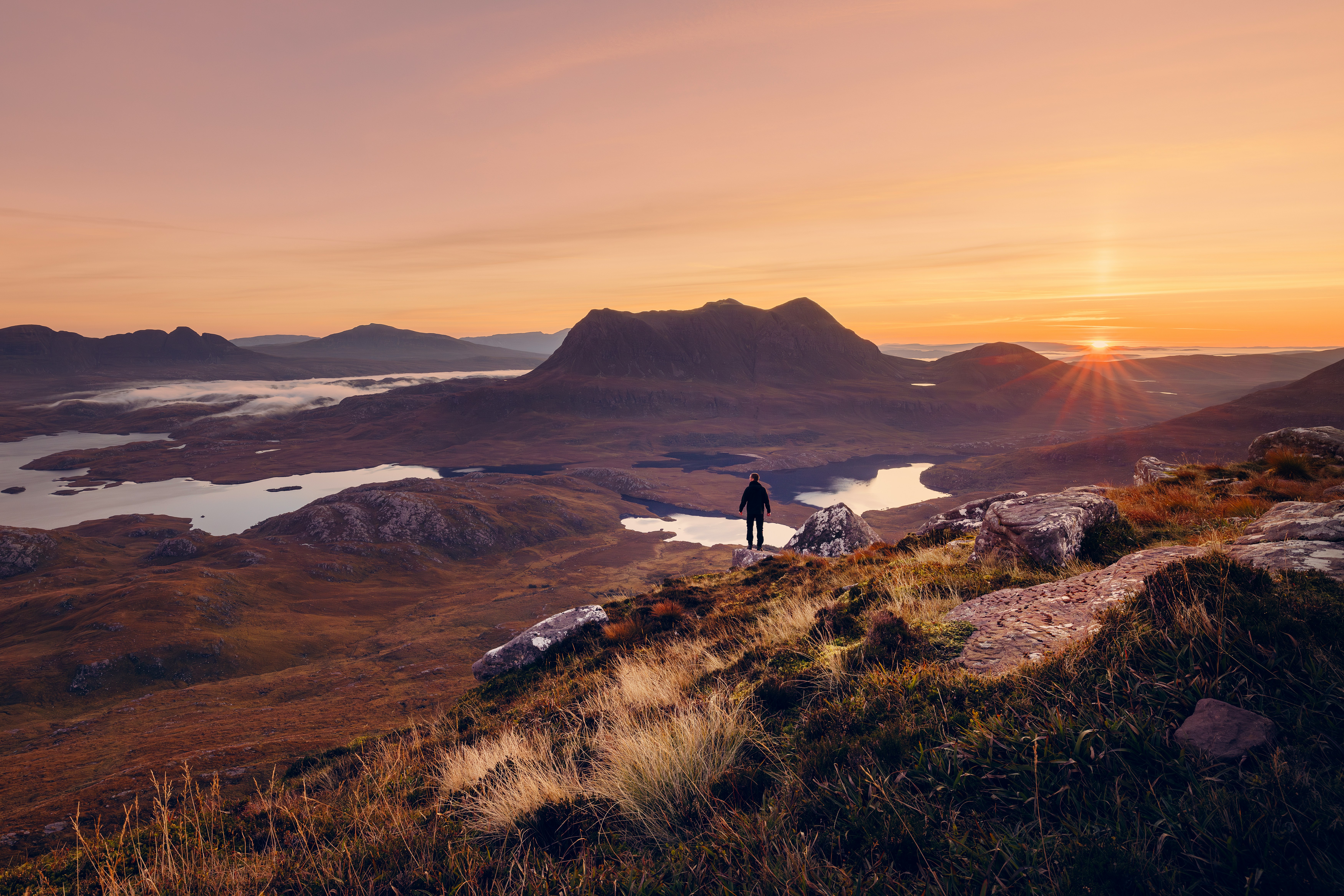 Wandelaar kijkt uit over een berglandschap bij zonsopgang